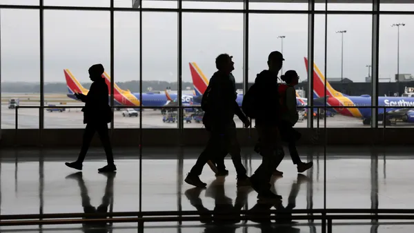 Travelers walk through an airport. The window behind them show Southwest Airlines airplanes sitting on the tarmac.
