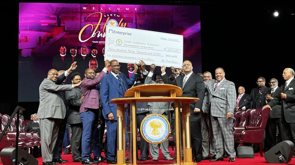 More than a dozen Church of God in Christ and Enterprise Community Partners representatives raise a giant check in the air to mark the launch of an affordable housing initiative.