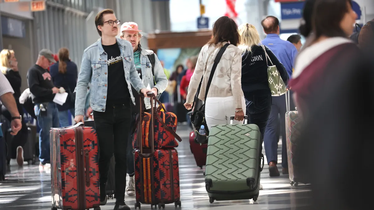 People walk with luggage through a busy terminal.