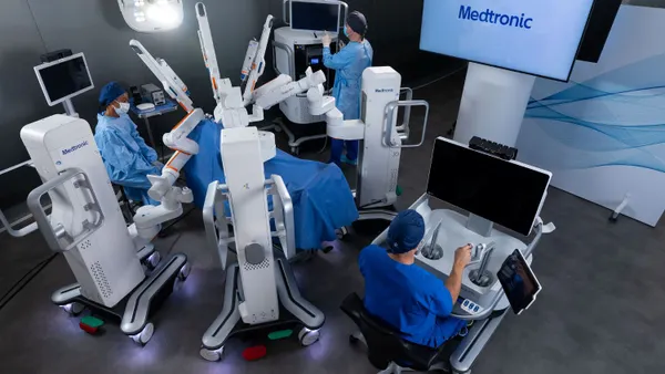 Three clinicians work with a robotic surgery system as a patient lies on the operating table.