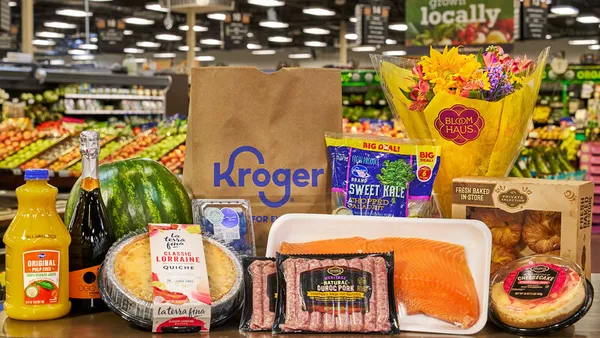 Grocery items including quiche, orange juice, a floral bouquet and sweet kale, on a table at a grocery store.