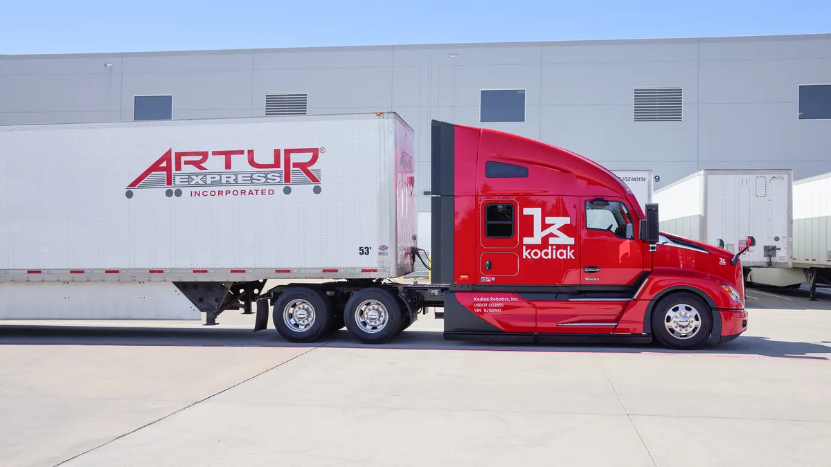 A Kodiak self-driving truck and Artur Express trailer outside a building in a parking area.