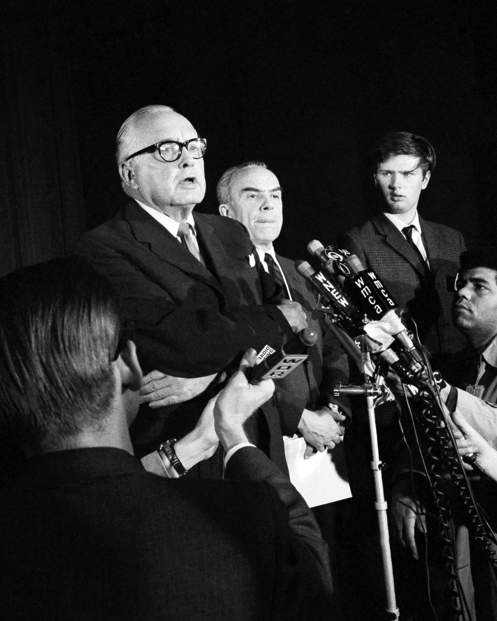 A person speaks into several microphones during a news conference.