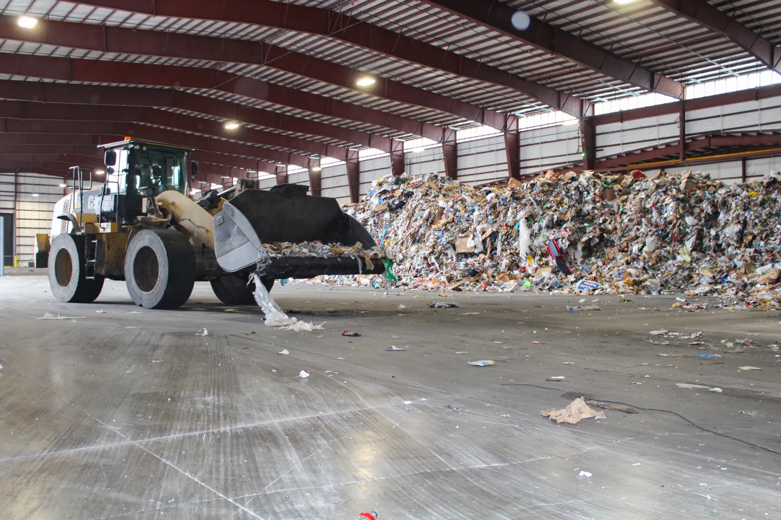 A front enloader moves recyclables into piles in a warehouse where material is stored.