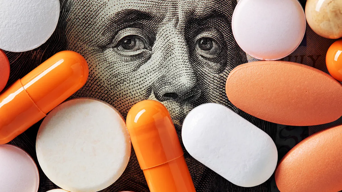 A number of colorful pills cover a 100 dollar bill surrounding the photo of Ben Franklin's face.