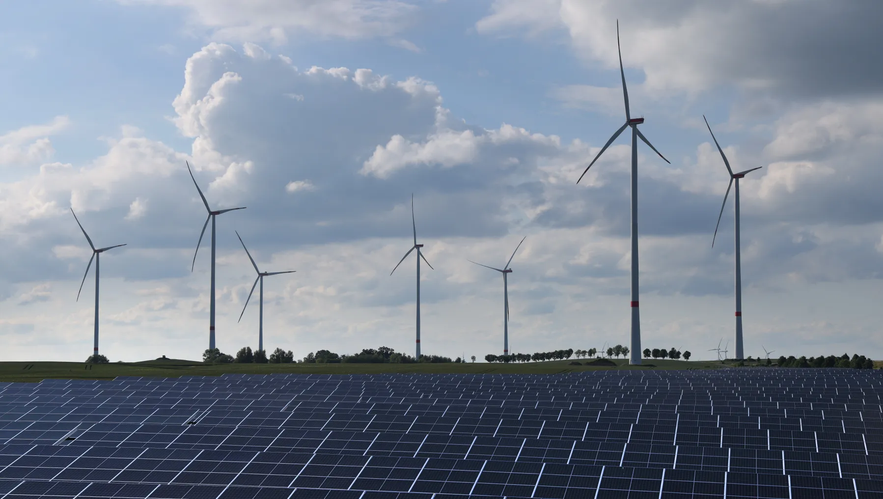 Wind turbines spin behind a solar energy park.