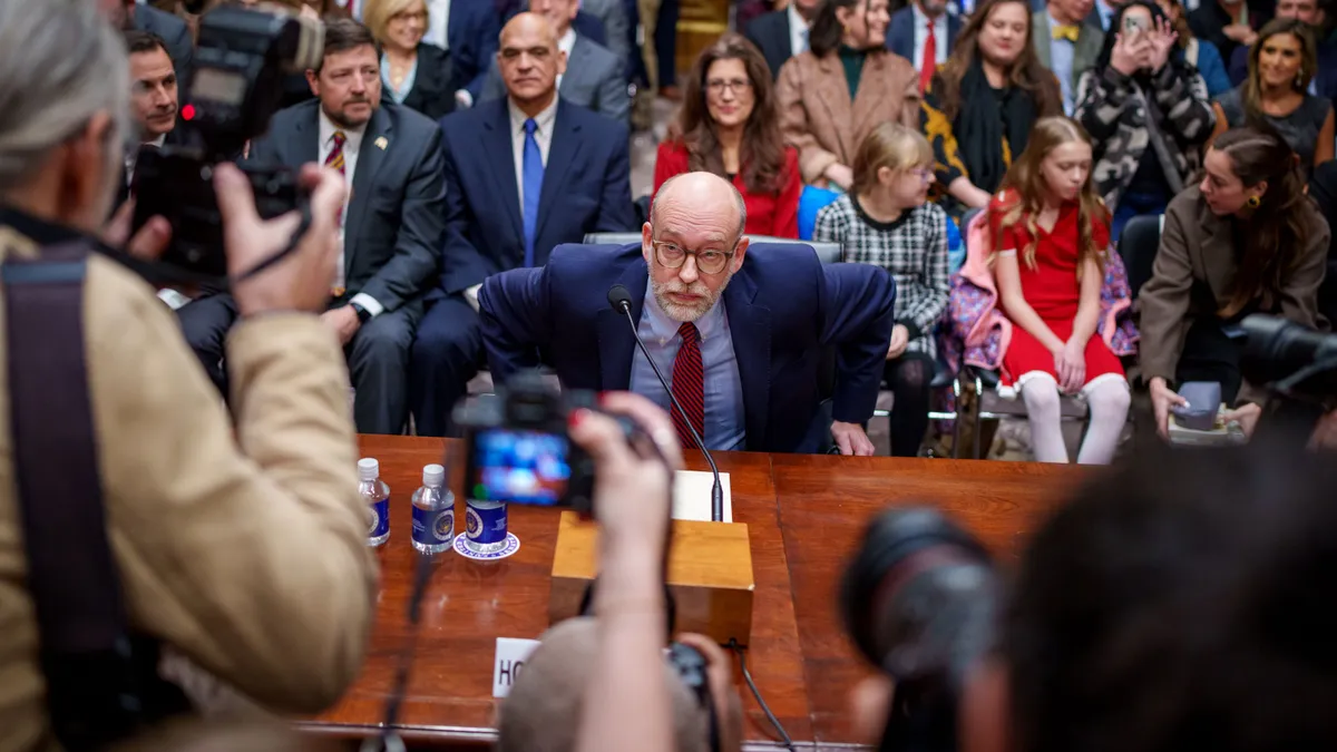 A man sits at a table as photographers stand over him.