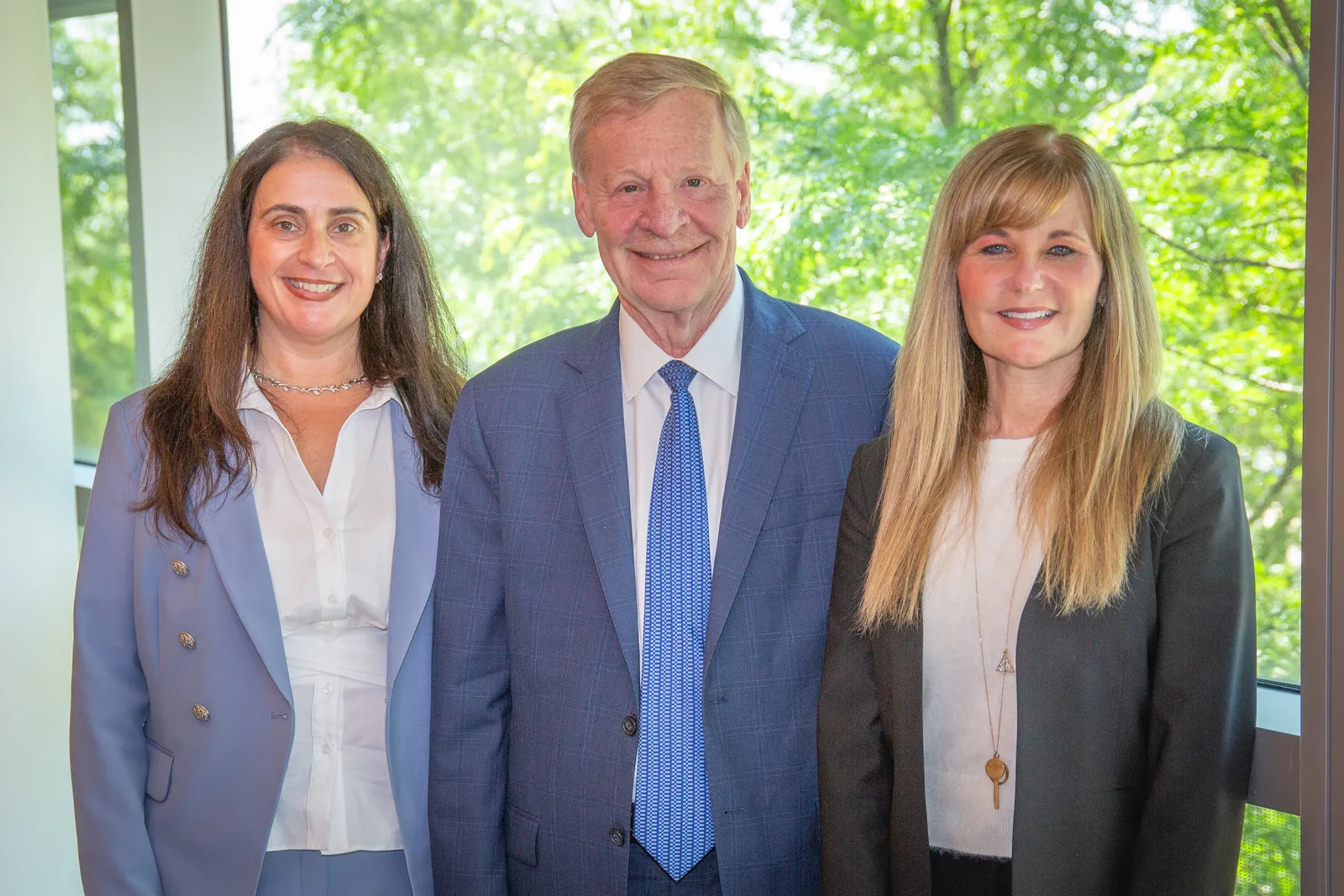 Three people in business attire with a trees in the background.