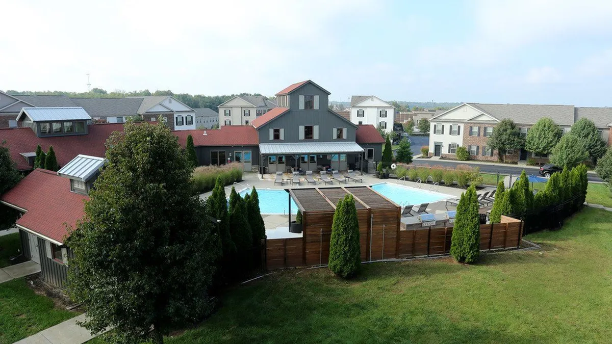 Brown apartments surrounding a pool with grass in the foreground.