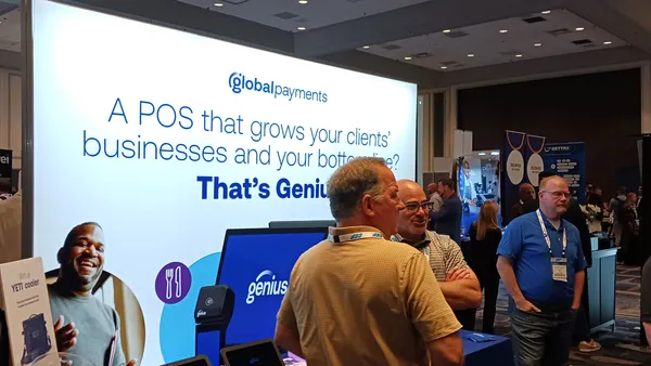People mill at a conference with a Global Payments sign that markets its Genius brand in the background.