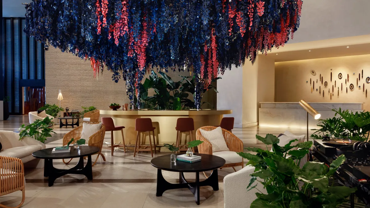 Pink and purple flowers hang from the ceiling in a hotel lobby.