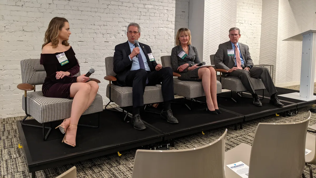 FERC Chair Richard Glick speaking on a stage, seated besides SEIA's Gizelle Wray and former commissioners Suedeen Kelly and Tony Clark.