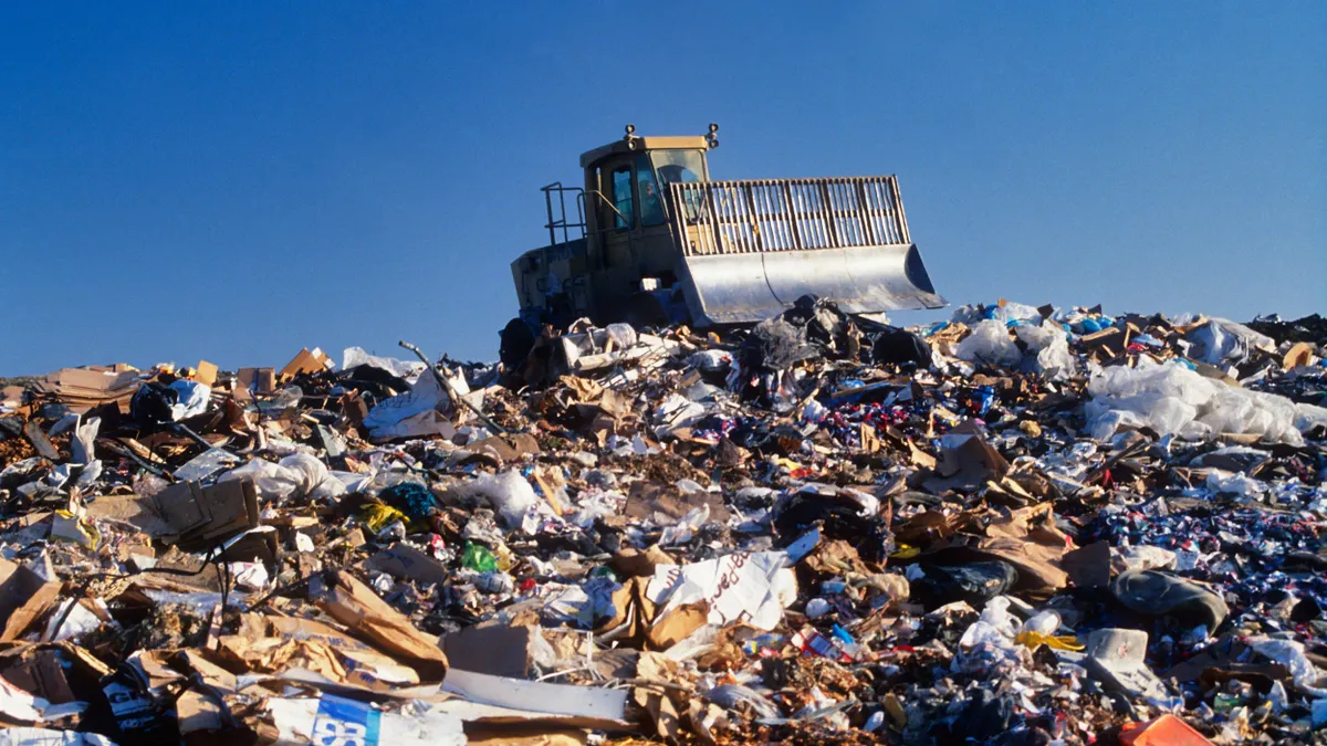 A bulldozer dits above a massive mound of mixed trash in a landfill. 