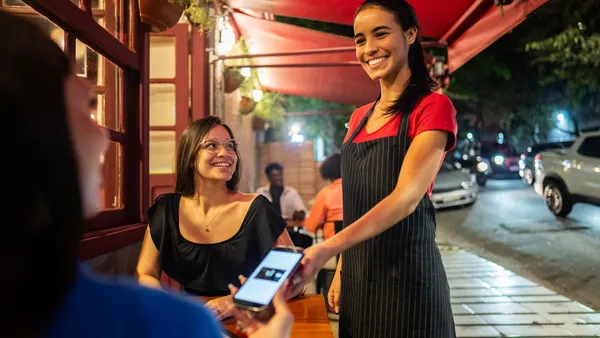 Waitress attending customers and using mobile phone in a restaurant