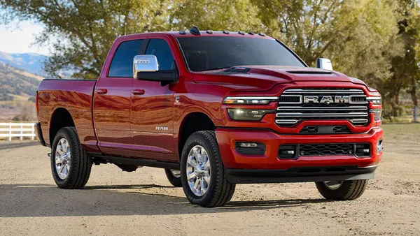 A red 2025 Ram 2500 pickup parked outdoors with a white fence in the background.