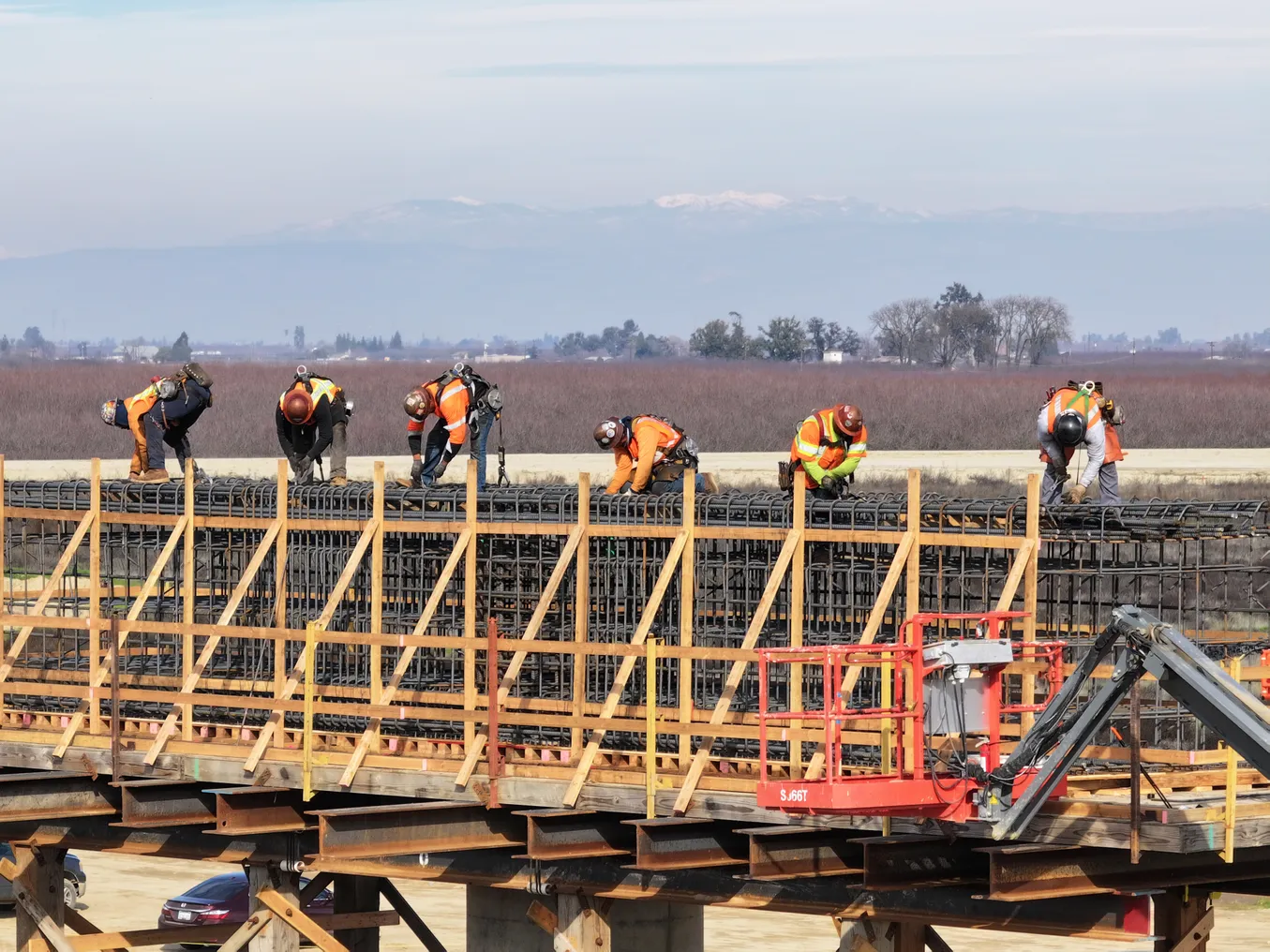 Six construction workers stand on rebar along a viaduct.