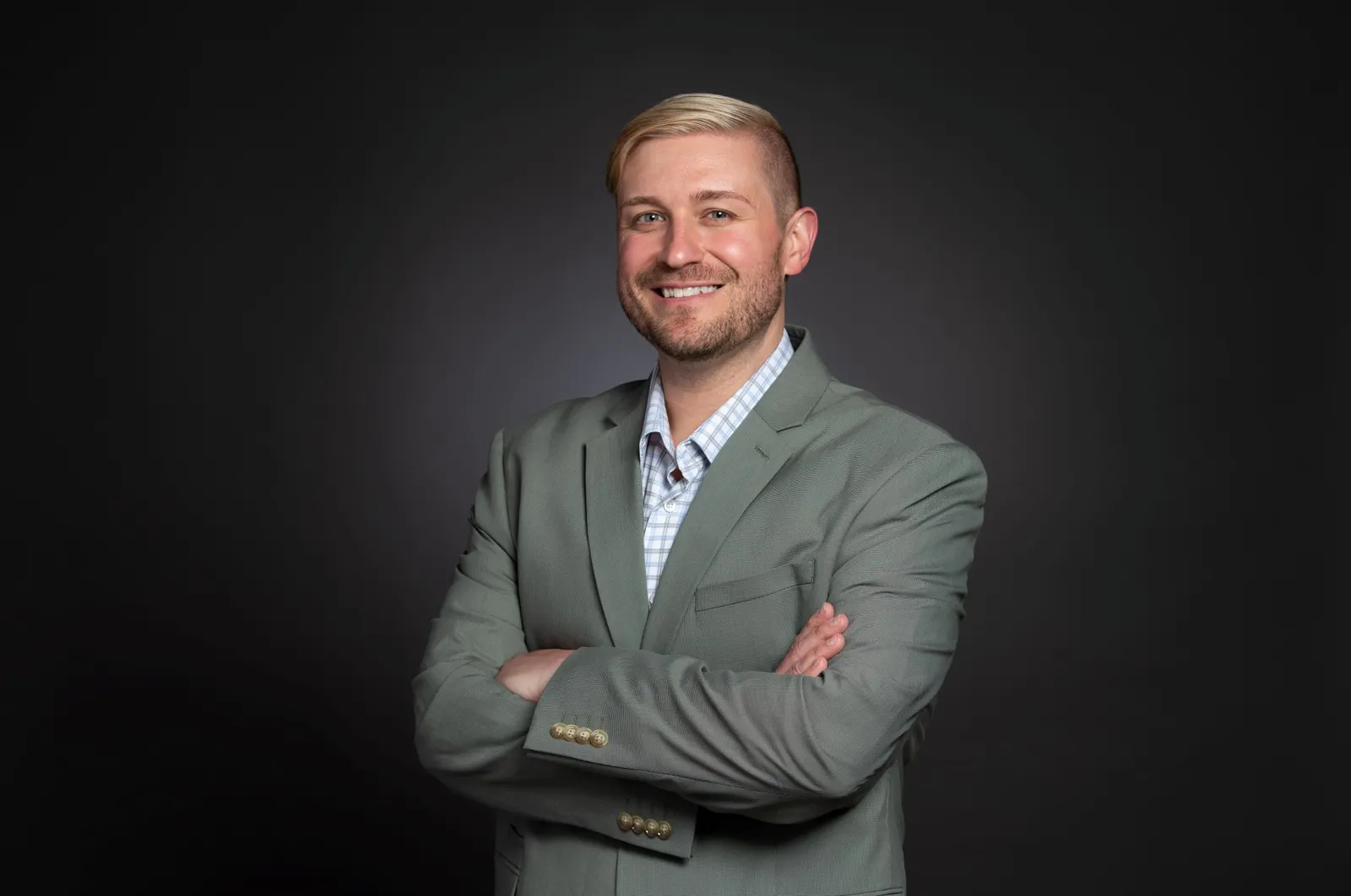 Headshot of a man with blonde hair, arms crossed in a light gray suite against a charcoal gray backdrop