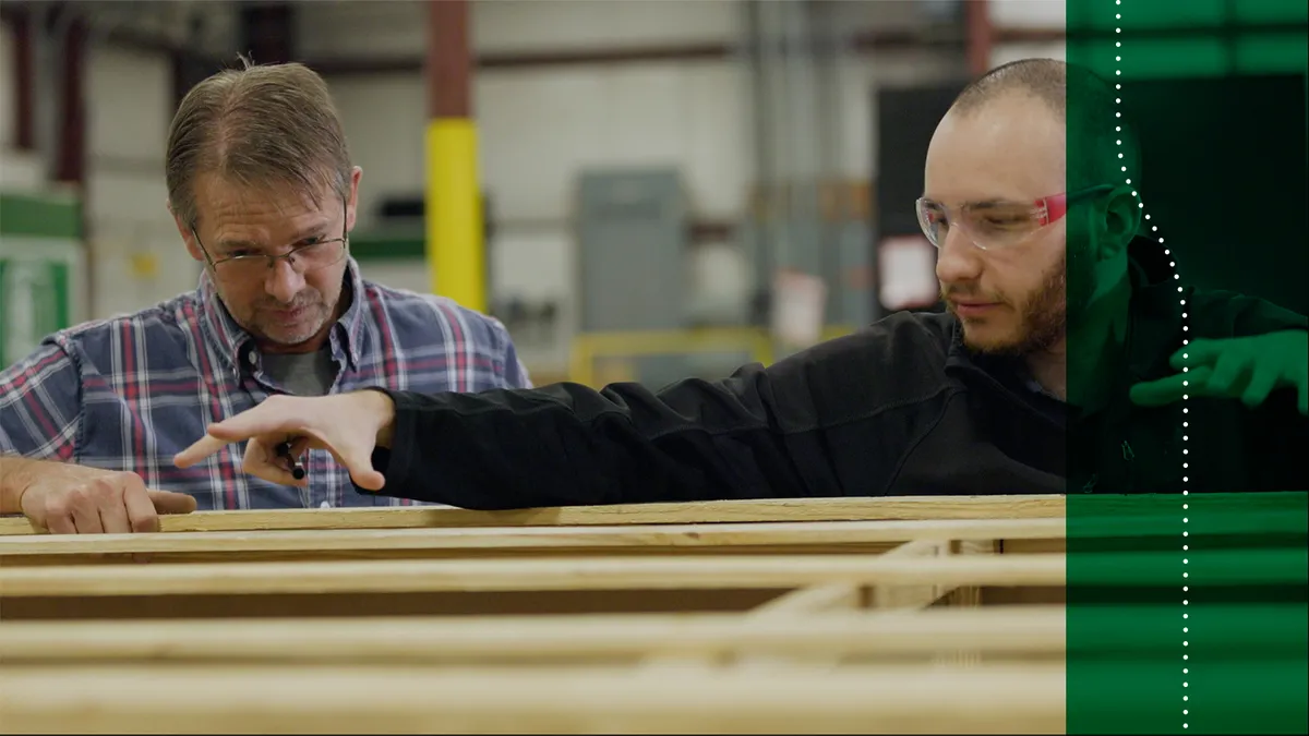 Two men stand over wooden packaging boxes and discuss dimensions