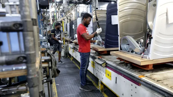 Two people wearing protective goggles and gloves working on an appliance production line.