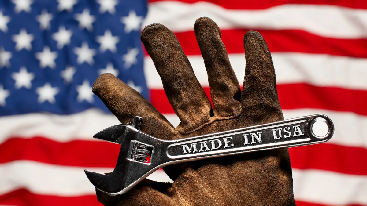 A brown, worn work glove holding a wrench that has "Made in USA" text on it, and the U.S. flag in the background.