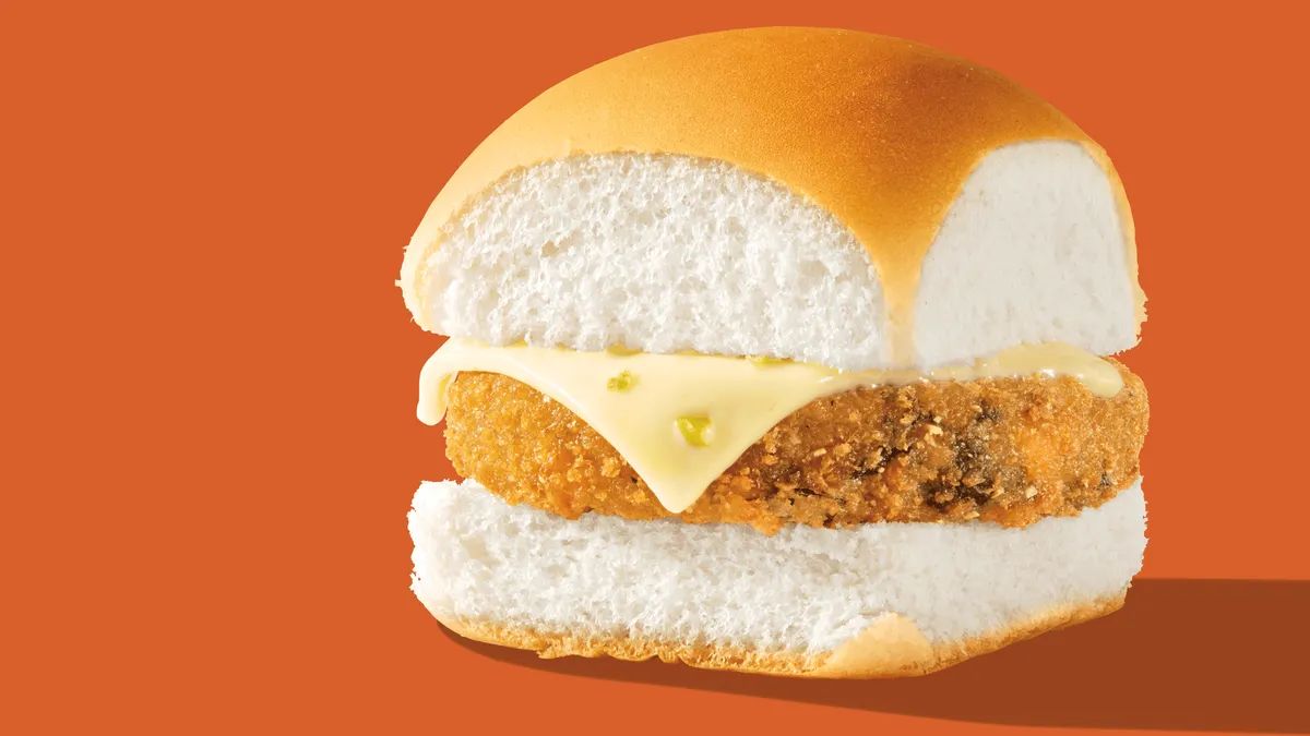A close up image of a veggie slider with white bun and jalapeno cheese. There is a orange background