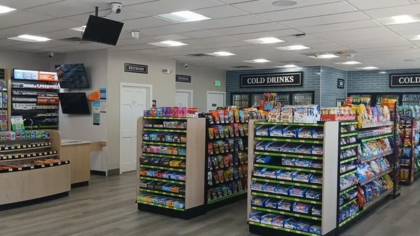 A photo of the inside of a store. Signs on the wall say "cold drinks" over a bank of coolers and "Restroom" over two doors in the back. Shelves of snacks are in the middle of the field.