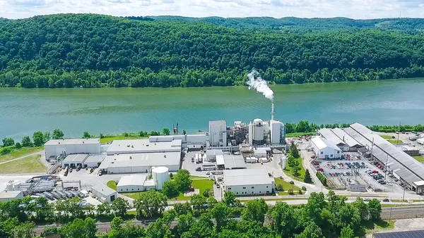 Aerial view of an industrial facility with a smokestack on the bank of a river.