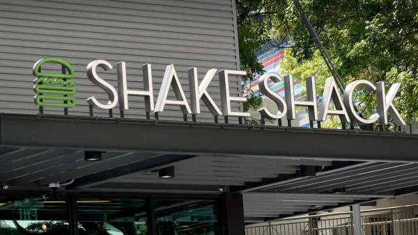 An image of a store sign that says Shake Shack. To the left is a green neon sign of a burger