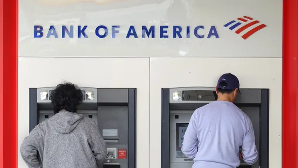 Two people with their backs to the camera use Bank of America ATMs.