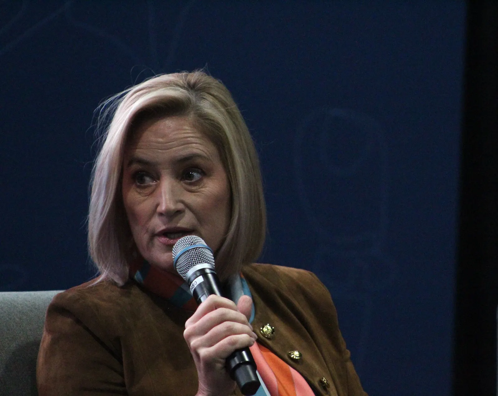 A person looks to the side and speaks holding a microphone.