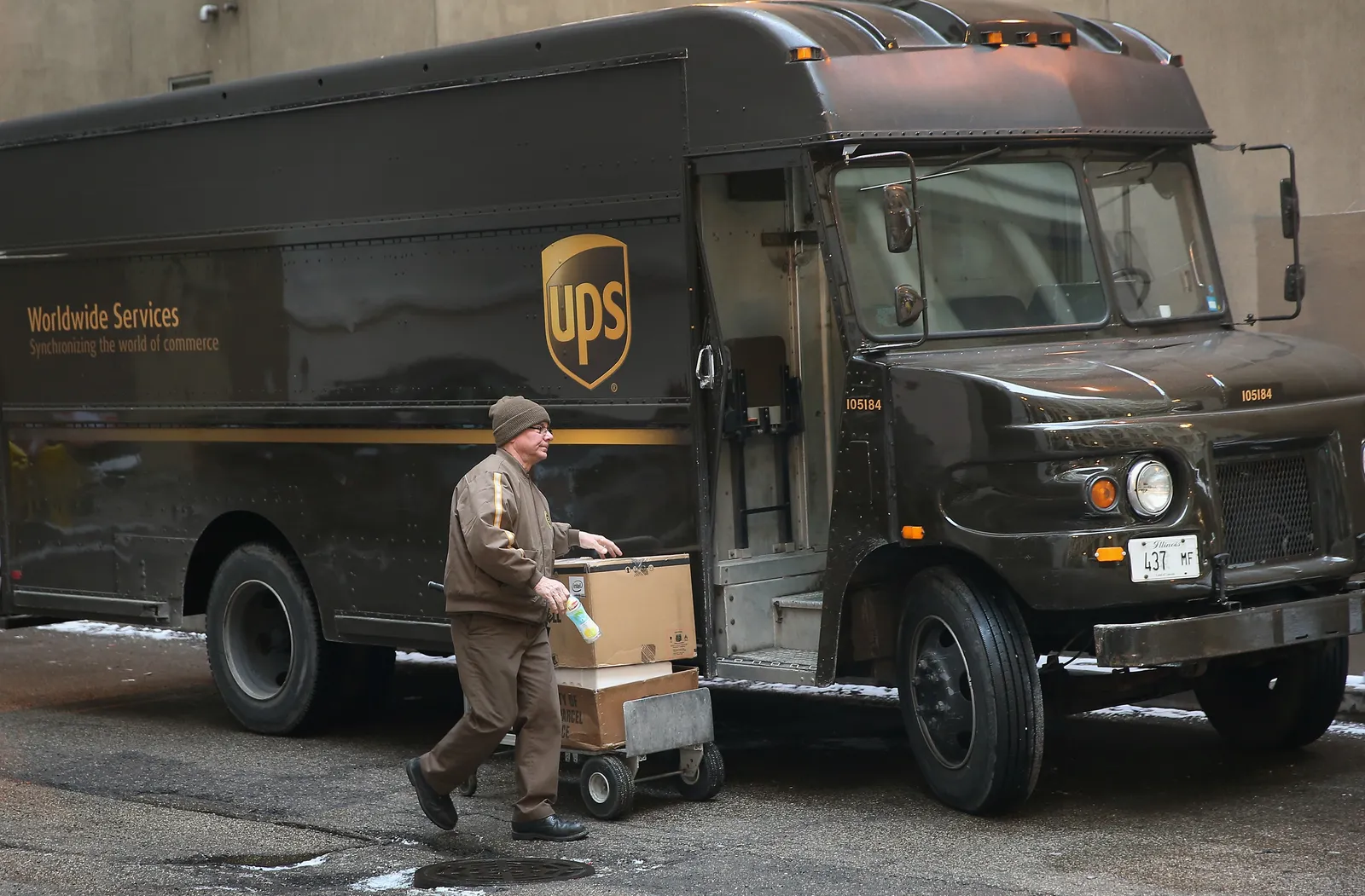 A UPS worker moves packages next to a delivery truck.