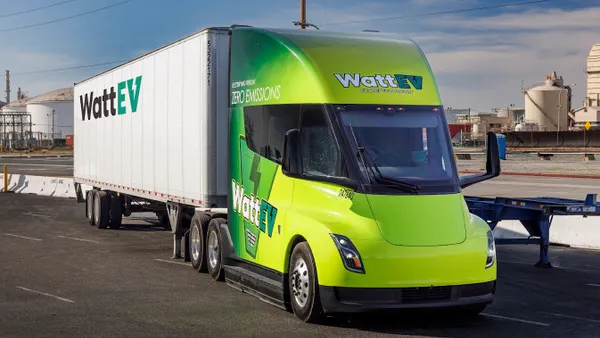 A WattEv tractor-trailer parked next to concrete barriers.