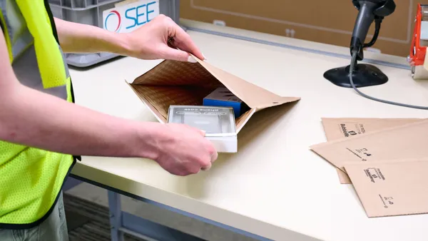 A person opens a fiber e-commerce mailer and places an item inside.