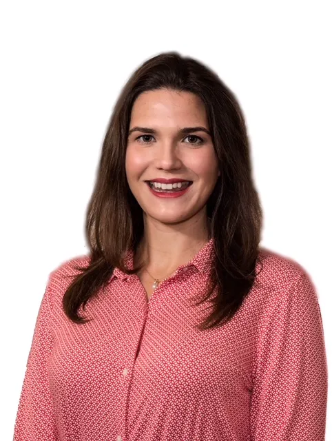 A headshot of a smiling women with long brown hair in a pink blouse.