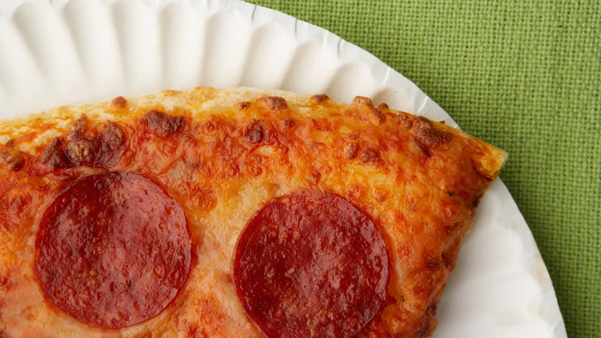 Partial view of pizza with pepperoni and cheese on a white paper plate