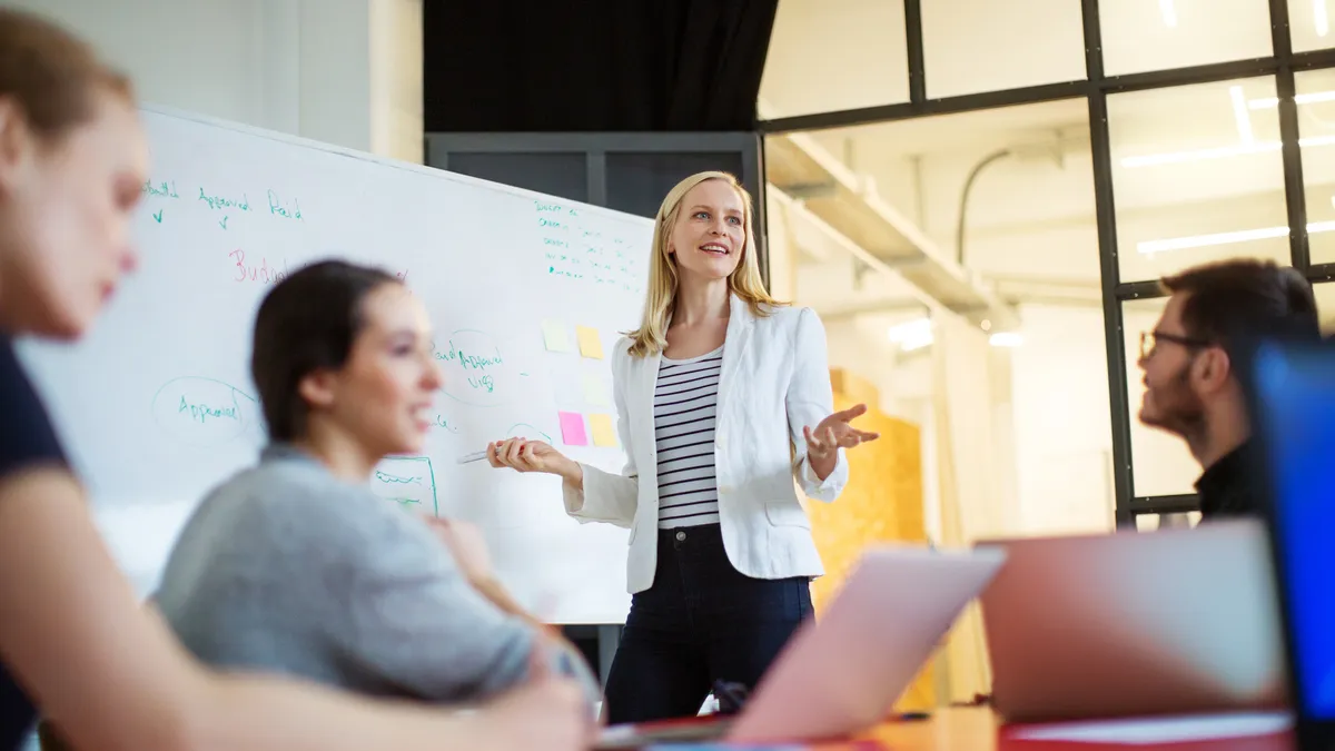 A woman leading a group office session by a whiteboard.