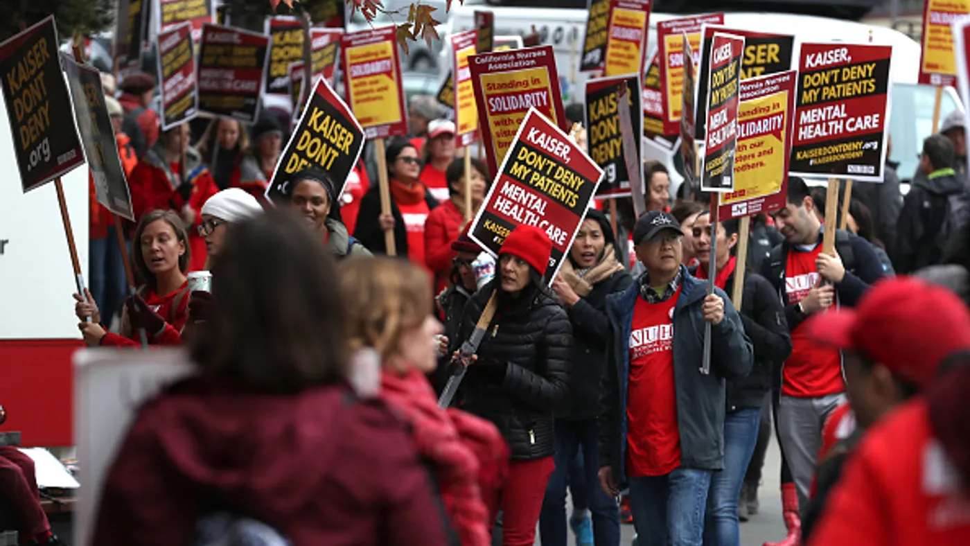 Kaiser Permanente mental health workers on strike carry signs