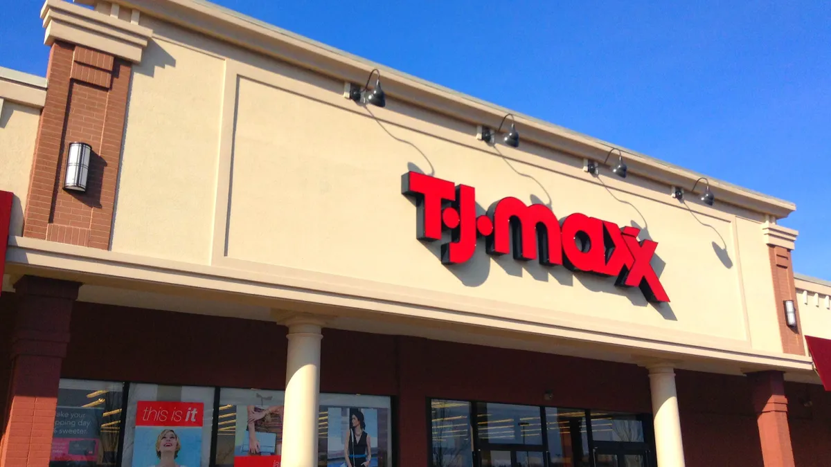 A beige stone and brick storefront reads "TJ Maxx" in bright red letters, against a bright blue sky.