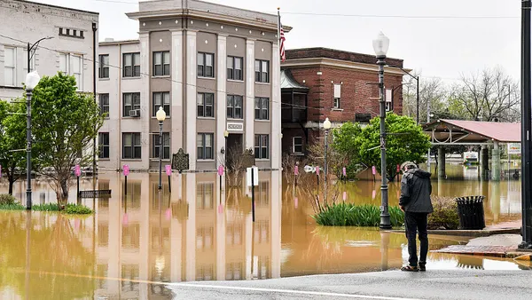 A persong in a coat overlooks a flooded city block of businesses.