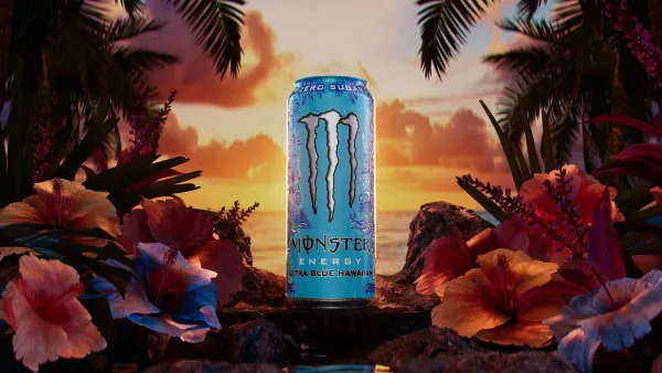 A photo of a can of energy drink on a rock near the ocean with tropical plants on both sides. The can says Zero Sugar Monster Energy Ultra Blue Hawaiian.