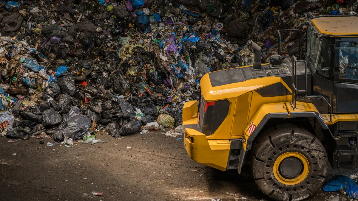 Piece of heavy equipment in front of large pile of garbage