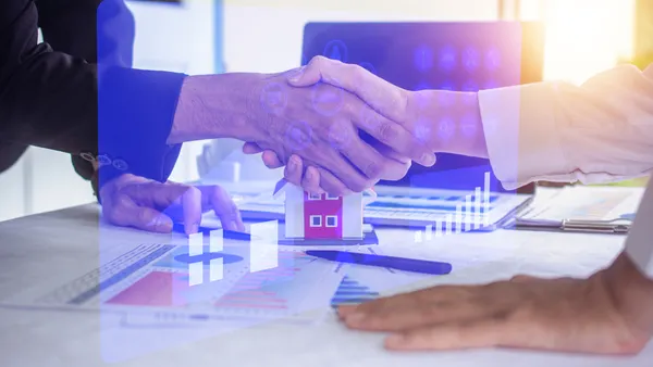 Closeup of a handshake with architectural drawings in the background.