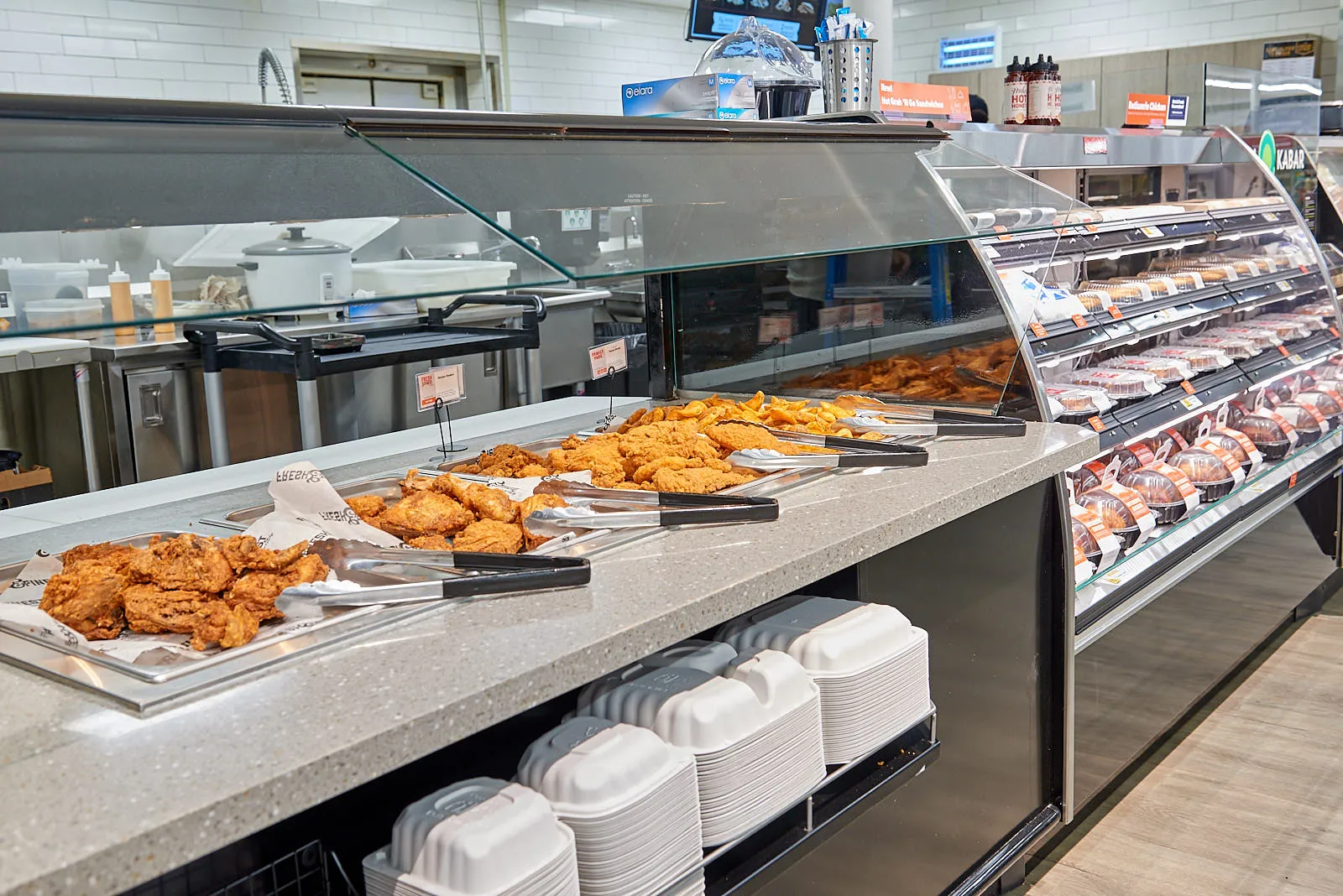 Hot-and-ready counter in grocery store offering serve-your-own fried chicken options and fries.