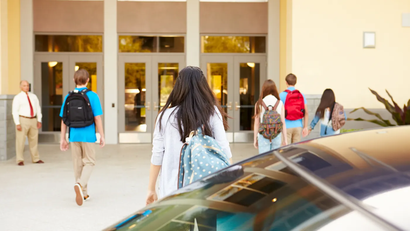 High school students are dropped off for school and begin walking into the building.