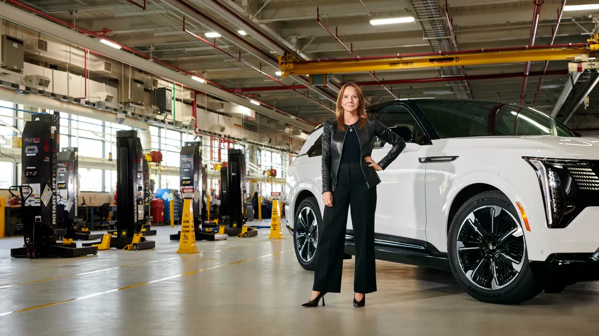 Mary Barra, General Motors Chair and Chief Executive Officer pictured stand in front of a Cadillac Escalade SUV in a dealership service facility..