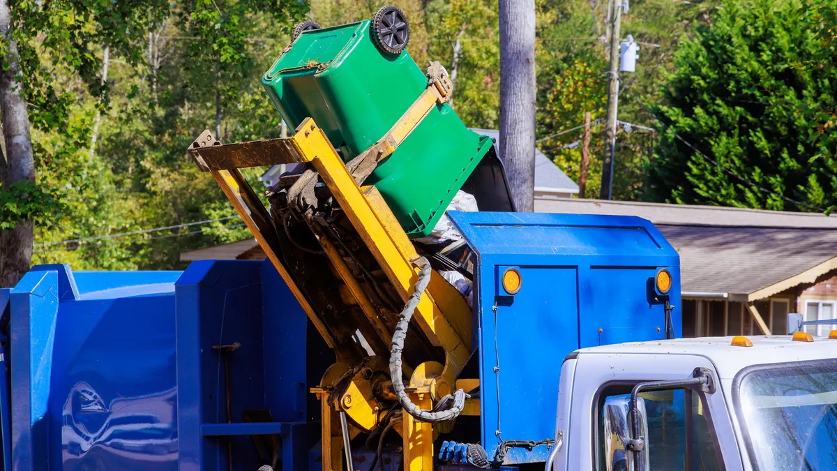 A blue collection truck tips a cart to unload it