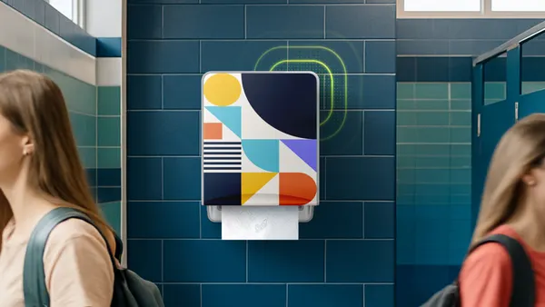 A modern paper towel dispenser with a colorful geometric design mounted on a dark blue tiled bathroom wall.