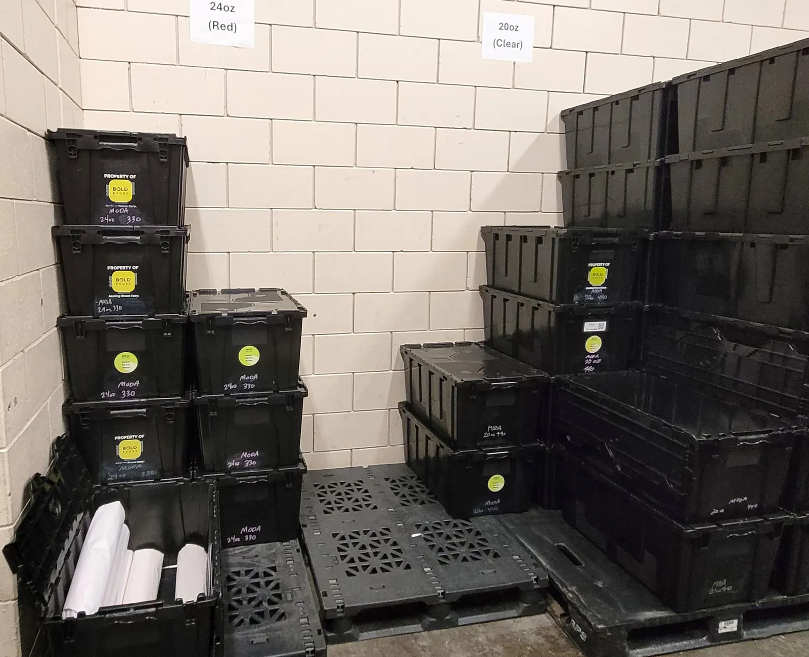 Rigid plastic totes are stacked on pallets in a room.