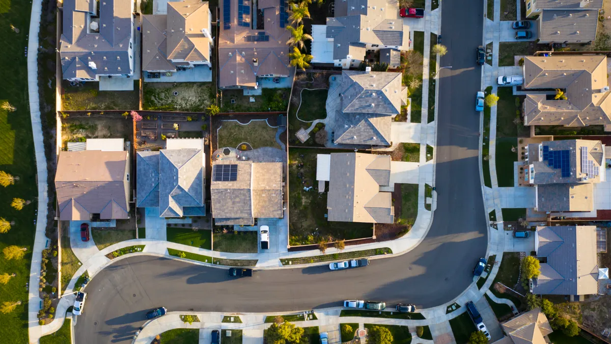 Aerial view of rooftops in a suburban neighborhood. A street curves through the houses.