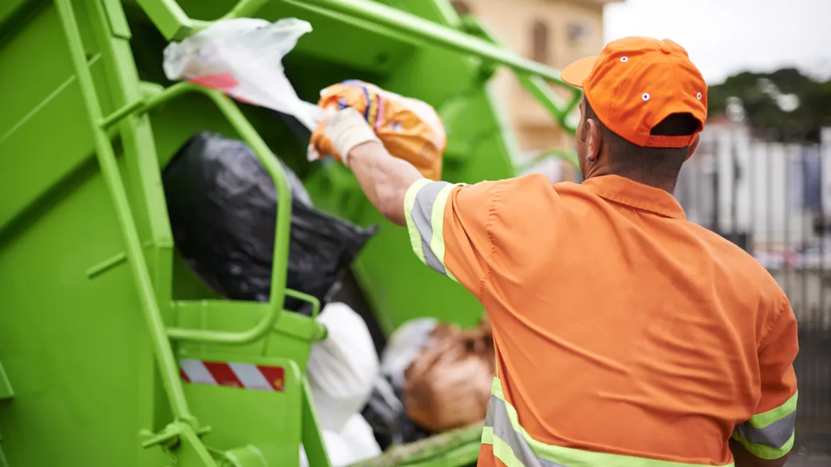 A waste and recycling collection worker tosses a bag into the back of a refuse truck.